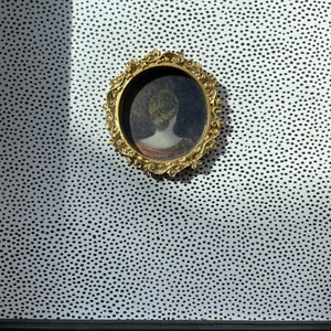 May include: A gold framed circular mirror with a black and white polka dot background.