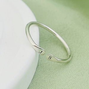May include: A silver ring with the letters "J" and "S" engraved on the sides. The ring is open on one side, making it adjustable.
