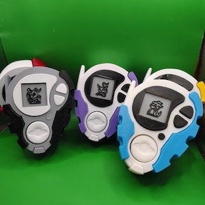 May include: Three colorful handheld digital devices with small screens displaying a pixelated creature. The devices have white, black, purple, and blue accents. Each device has a central button and a circular screen.