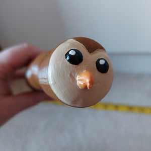 Puede incluir: Una figurita de búho marrón y blanco con ojos negros y un pico naranja. El búho está pintado con un estilo realista.