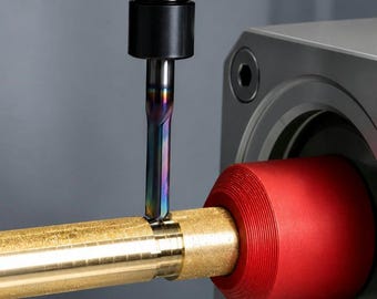 Può includere: Un utensile di fresatura in metallo con finitura iridescente sta tagliando un'asta di ottone orizzontale. L'asta è fissata da un dispositivo cilindrico rosso brillante collegato a un alloggiamento meccanico grigio, mostrando un processo di lavorazione preciso.