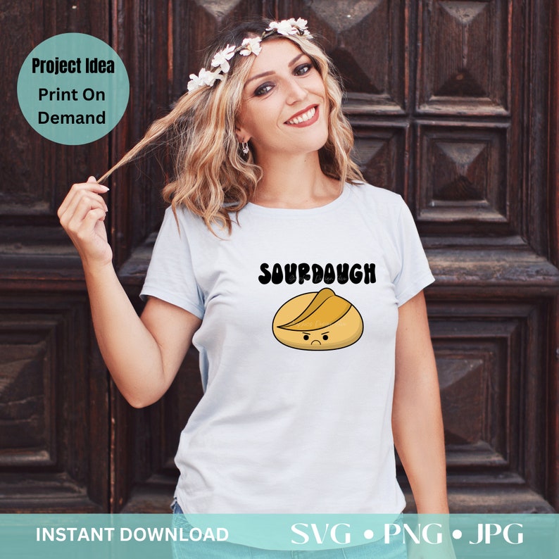 Pode incluir: Uma camiseta azul clara com a palavra "SOURDOUGH" acima de um desenho animado de p&atilde;o de massa madre com uma express&atilde;o carrancuda. A imagem tamb&eacute;m inclui o texto "Project Idea Print On Demand" e "INSTANT DOWNLOAD SVG &bull; PNG &bull; JPG".