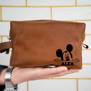 May include: Brown leather toiletry bag with a black Mickey Mouse design and the name "ALEX" printed on the front.