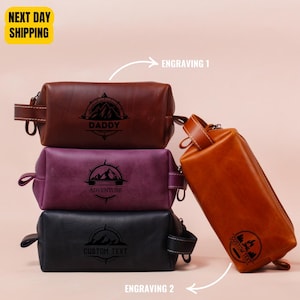May include: Three leather toiletry bags stacked on top of each other. The top bag is brown and has the word "Daddy" engraved on it. The middle bag is purple and has the word "Adventure" engraved on it. The bottom bag is black and has the words "Custom Text" engraved on it.