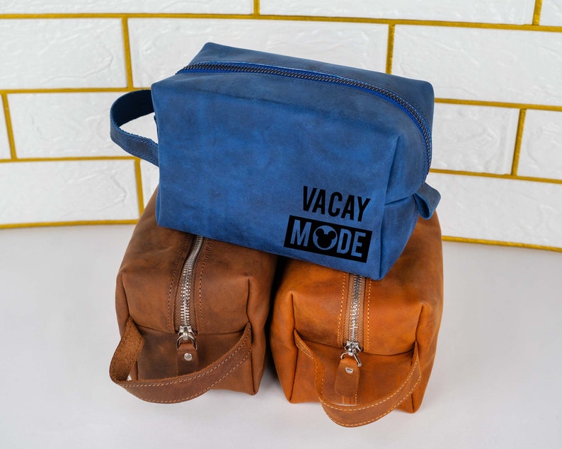 May include: Three toiletry bags, one blue and two brown. The blue bag has the text "VACAY MODE" with a Mickey Mouse head icon.