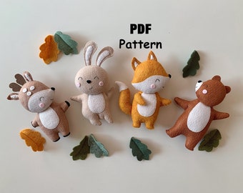 May include: A PDF pattern featuring four felt animal plushies: a deer, a rabbit, a fox, and a bear. Each animal has a white belly, pink cheeks, and stitched facial features. The set includes several small felt oak leaves in orange and green.