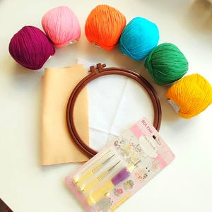 Pode incluir: Um kit de artesanato com novelos de lã coloridos em rosa, laranja, azul, verde e amarelo. Inclui um bastidor de bordado de madeira, tecido e um conjunto de agulhas de perfuração. Ideal para bordados e trabalhos têxteis.