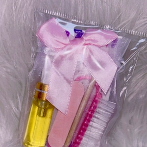 May include: A clear plastic bag filled with a pink bow and various nail care items, including a nail file, a cuticle pusher, a nail brush, and a small bottle of oil.