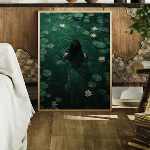 May include: A framed print of a woman swimming in a pond with white water lilies. The water is a deep green color and the woman's long dark hair is flowing behind her.