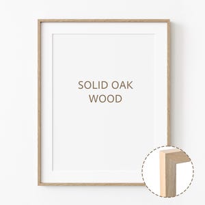 Könnte beinhalten: Ein Bilderrahmen aus Naturholz mit einem weißen Passepartout und dem Text "SOLID OAK WOOD" in brauner Farbe. Der Rahmen wird mit einer Nahaufnahme der Ecke gezeigt, um die Holzmaserung hervorzuheben.