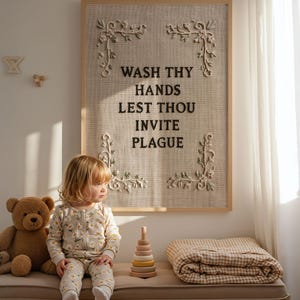 May include: A rectangular wall art piece featuring a light beige textured fabric background framed in light wood. The text WASH THY HANDS LEST THOU INVITE PLAGUE is embroidered in dark brown thread, accented by four cream-colored floral corner motifs.