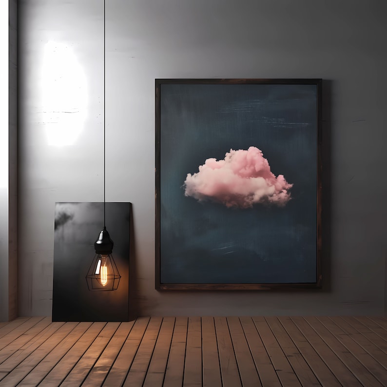 May include: A black framed picture with a pink cloud on a dark blue background hangs on a white wall. A black pendant light with a caged bulb hangs in front of a black and white picture on the wall.