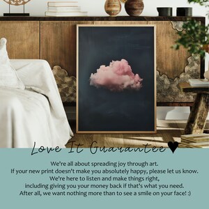 May include: A framed print of a pink cloud against a dark blue background. The print is in a gold frame and is hanging on a wall. The text "Love It Guarantee" is written in white letters on a light blue background below the print. The text reads: "We're all about spreading joy through art. If your new print doesn't make you absolutely happy, please let us know. We're here to listen and make things right, including giving you your money back if that's what you need. After all, we want nothing more than to see a smile on your face! :)"