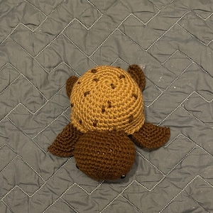 May include: A crocheted brown and tan turtle toy. The turtle has a brown body and a tan shell with brown spots.