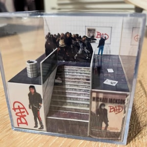 Könnte beinhalten: Miniatur-Diorama in einer transparenten Acrylbox, das eine U-Bahn-Szene mit Figuren und Treppen zeigt. Plakate mit dem Wort "BAD" und einem Michael Jackson Albumcover sind zu sehen.