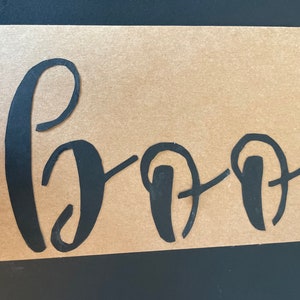 May include: A brown paper card with the word "Boo" written in black cursive lettering.