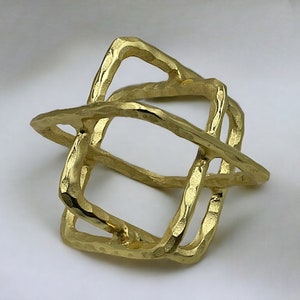 May include: A gold-colored metal sculpture in the shape of a cube with an open, geometric design. The sculpture has a rough, textured surface.