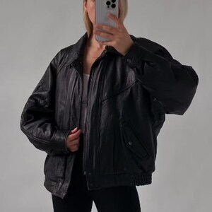 May include: A black leather bomber jacket with a zipper closure and a ribbed collar. The jacket has a pocket on the left side and a zippered pocket on the right side.