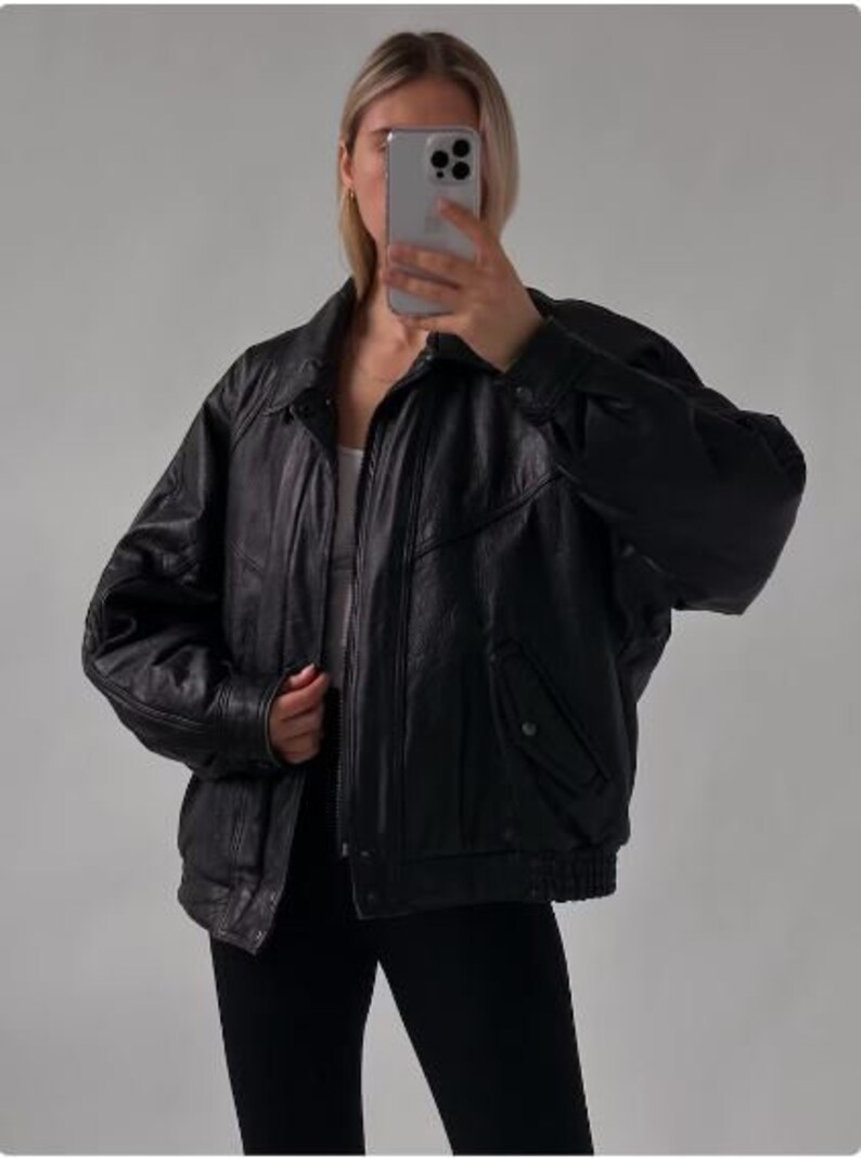 May include: A black leather bomber jacket with a zipper closure and a ribbed collar. The jacket has a pocket on the left side and a zippered pocket on the right side.