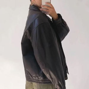 May include: A black leather jacket with a zipper closure and a ribbed waistband. The jacket has a relaxed fit and a slightly cropped length.