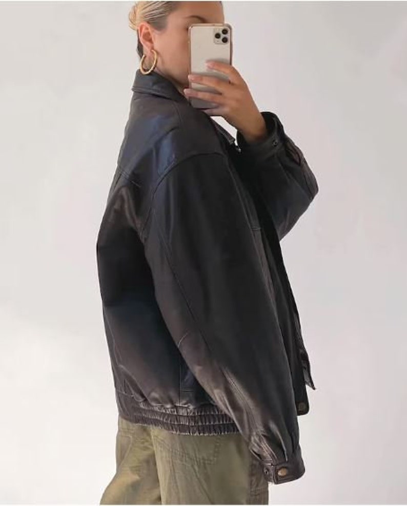 May include: A black leather jacket with a zipper closure and a ribbed waistband. The jacket has a relaxed fit and a slightly cropped length.