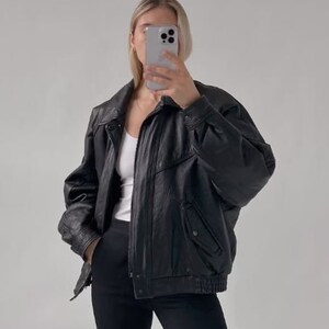 May include: A black leather jacket with a zipper closure and a stand-up collar. The jacket has a zippered pocket on the left side and a snap closure at the bottom.