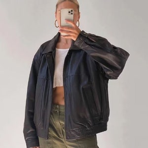 May include: A black leather jacket with a zipper closure and multiple pockets. The jacket has a relaxed fit and a slightly oversized silhouette.