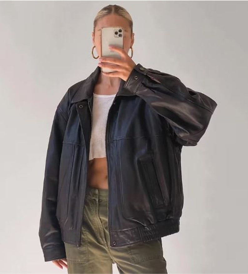 May include: A black leather jacket with a zipper closure and multiple pockets. The jacket has a relaxed fit and a slightly oversized silhouette.