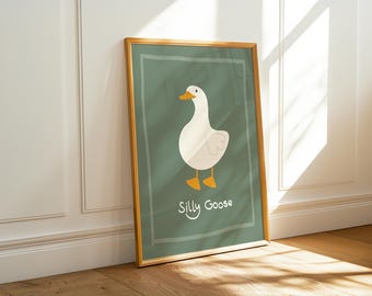 May include: A framed art print featuring a cartoon goose on a green background. The goose is white with orange feet and a beak. The words "Silly Goose" are written in a playful font at the bottom of the print. The frame is a light brown color.
