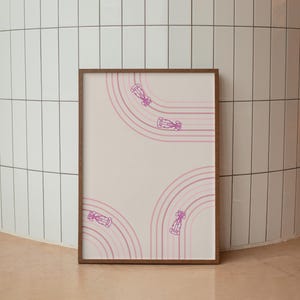 May include: A framed art print featuring a minimalist design of race cars on a track. The artwork showcases pink race cars and curved track lines against a cream background. The frame is a warm brown color.