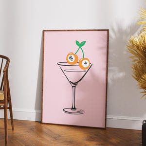 May include: A pink framed print with a black line drawing of a martini glass with two orange billiard balls as cherries on top. The billiard balls are numbered 8 and 4.