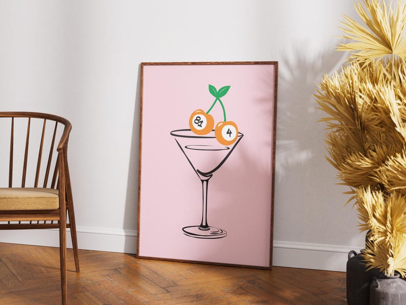 May include: A pink framed print with a black line drawing of a martini glass with two orange billiard balls as cherries on top. The billiard balls are numbered 8 and 4.