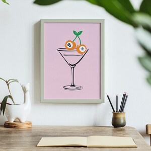 May include: A pink framed print with a black line drawing of a martini glass with two cherries on top. The cherries are numbered 8 and 4.
