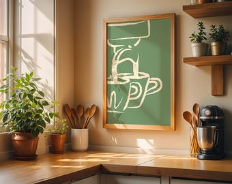 May include: A framed green and white coffee art print hangs above a wooden countertop. The print features a minimalist illustration of coffee being poured into two mugs. A coffee maker, wooden spoons, and potted plants are also visible.