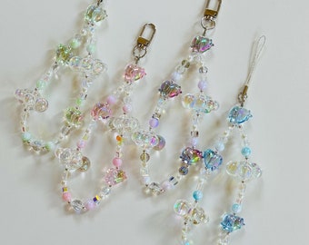 May include: Three iridescent charm phone straps with clear beads and iridescent heart charms. The charms are in shades of pink, blue, and green.