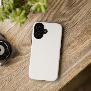 Può includere: Una cover per smartphone bianca a tinta unita con un ritaglio nero per il modulo fotocamera, dotato di due aperture circolari per gli obiettivi e una piccola apertura per il flash. La cover presenta una finitura liscia e opaca.