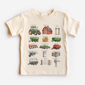 May include: A cream-colored short-sleeve t-shirt featuring a grid of colorful farm-themed illustrations. The graphic includes a green tractor, red barn, silo, grain cart, hay bale, trailer, plow, cultivator, baler, wheelbarrow, milk can, crate, water tank, fence, and windmill, each labeled with its corresponding name in black text.