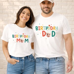 Puede incluir: Dos camisetas blancas de manga corta con un estampado gráfico colorido. El texto dice BIRTHDAY MOM y BIRTHDAY DAD, con la letra A reemplazada por un bebé con un gorro de fiesta. El diseño incluye pequeños puntos multicolores dispersos.