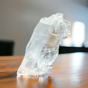Puede incluir: Un gran cristal transparente claro con una superficie rugosa e irregular. El cristal está sobre una superficie de madera.