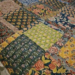 May include: A patchwork quilt with a mix of floral and geometric designs in blue, green, yellow, and pink. The quilt is constructed from numerous fabric squares, creating a textured and colourful design. The overall theme is a cosy, handmade textile, perfect for a bed or sofa.