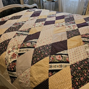 May include: A patchwork quilt with a variety of floral and geometric patterns in cream, tan, burgundy, and black. The quilt is displayed on a bed. The quilt is handmade.