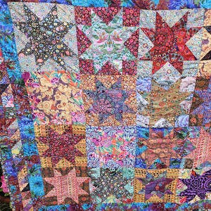 May include: A vibrant patchwork quilt with star motifs. The quilt showcases a range of floral and geometric fabric patterns in hues of blue, pink, red, and yellow. The quilt is constructed from numerous fabric squares stitched together.