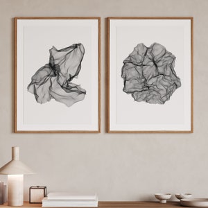 May include: Two framed black and white abstract art prints with a geometric design. The prints are in simple wooden frames and are hung on a light beige wall.