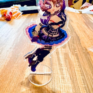 May include: A clear acrylic stand with a colorful anime character figurine. The character is wearing a black and purple outfit with a blue and pink skirt. The character has brown hair and blue eyes.