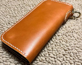 May include: A brown leather wallet with white stitching and a gold metal loop. The wallet is closed and lying on a light brown fuzzy surface.