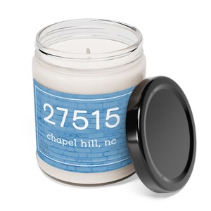May include: A glass jar candle with a black lid. The label is blue with white brick pattern and the text "27515 chapel hill, nc".