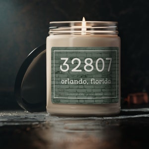 May include: A white candle in a glass jar with a green label. The label has a brick pattern and the text "32807 Orlando, Florida".