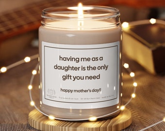 May include: A brown soy wax candle with a white label that reads "having me as a daughter is the only gift you need happy mother's day!!". The candle is lit and sitting on a wooden coaster.