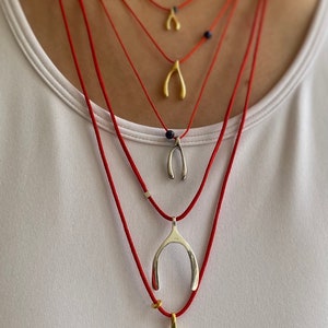 May include: A layered necklace with multiple red cords and silver and gold horseshoe charms. The charms are of varying sizes and are strung on the cords at different lengths.