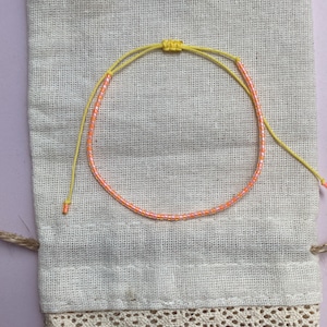 May include: A yellow and orange beaded bracelet on a white fabric pouch with lace trim.